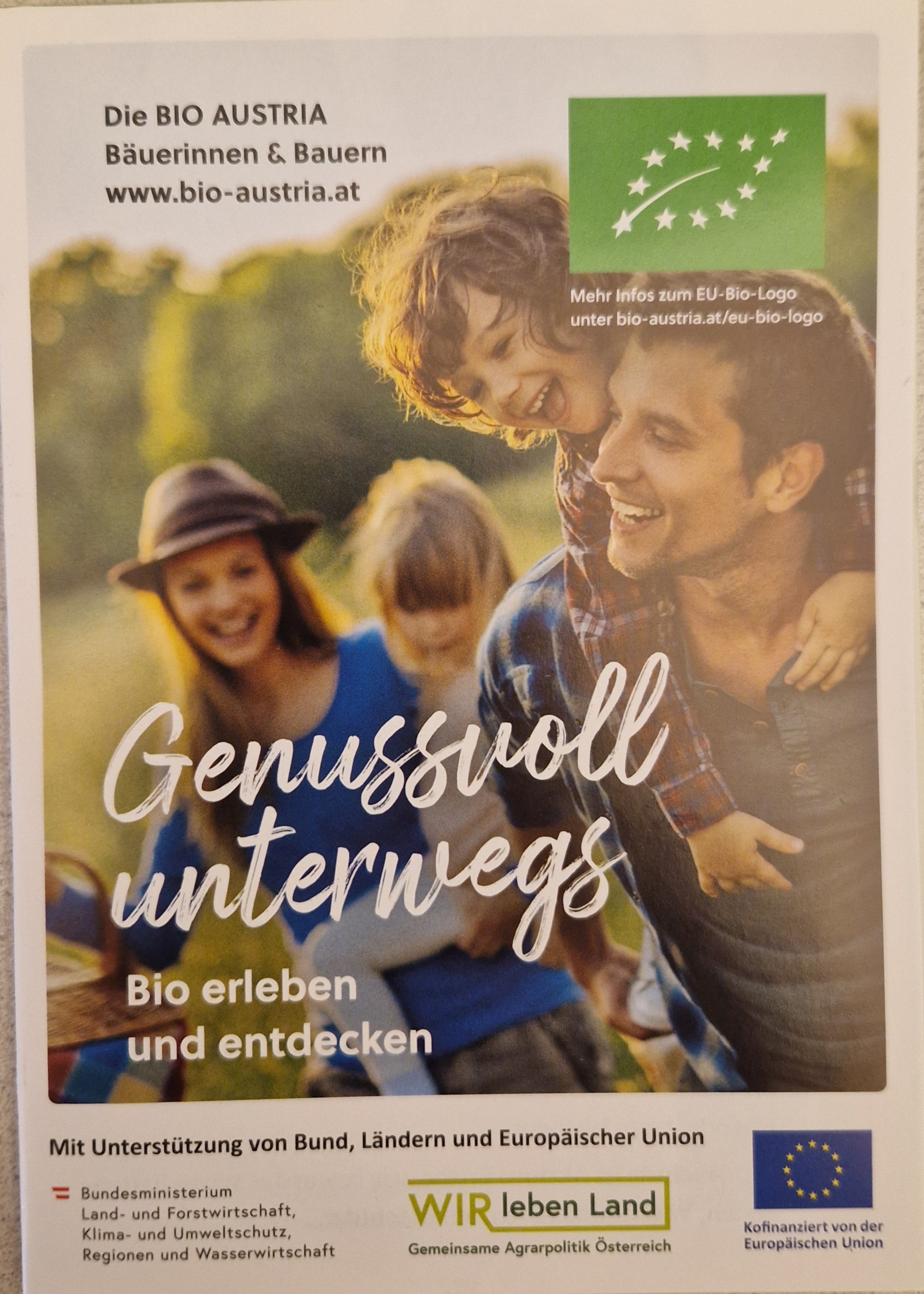 Titelbild_Genussvoll wandern Mann trägt Kind, huckepack dahinter lachende Frau mit Hut und Mädchen am Arm